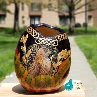 This vase features a portrait of a bird framed  by gold leaves and flanked by the Ghanaian Kente Cloth.