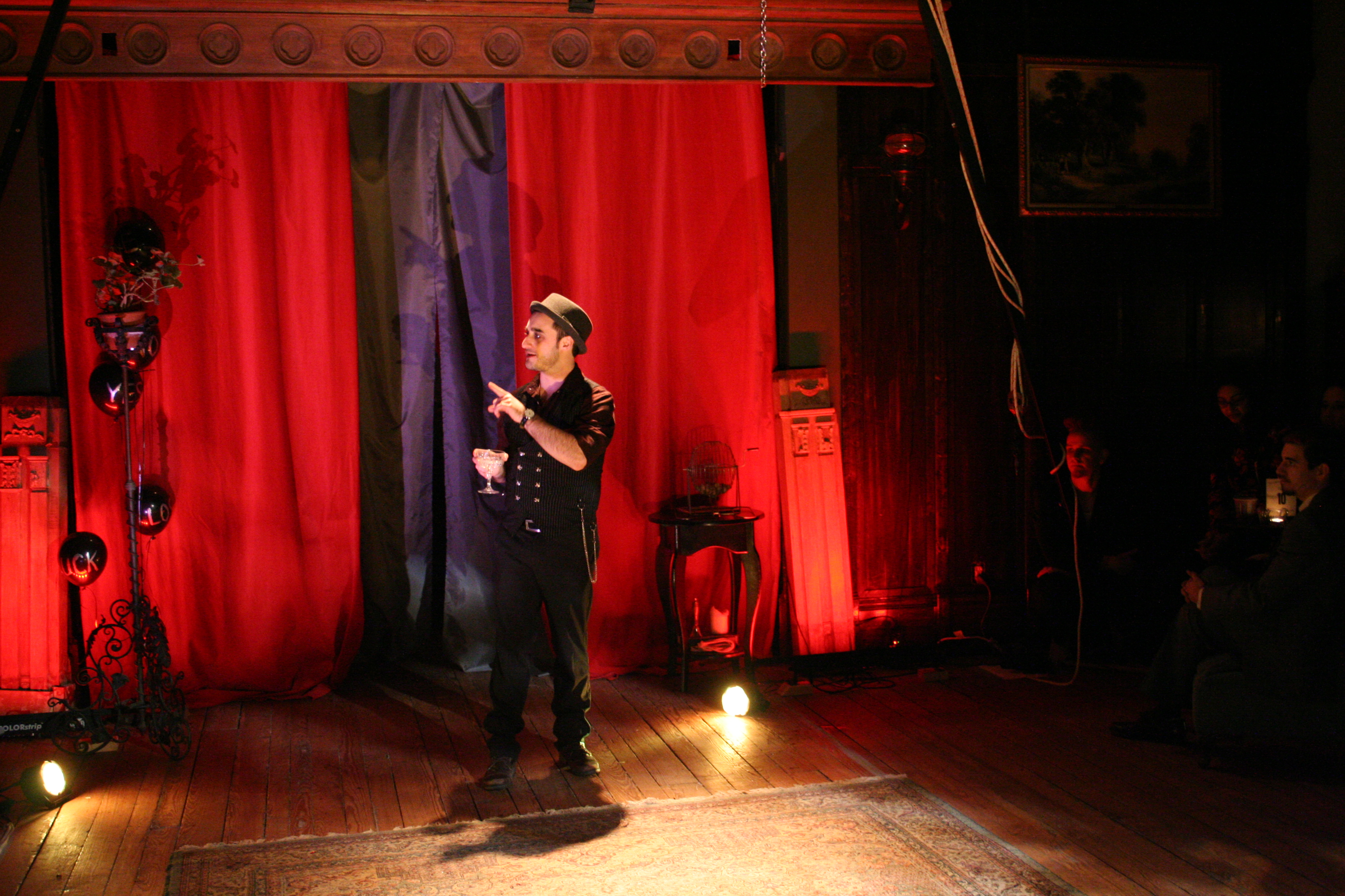 Magician stands center stage in front of red curtains.