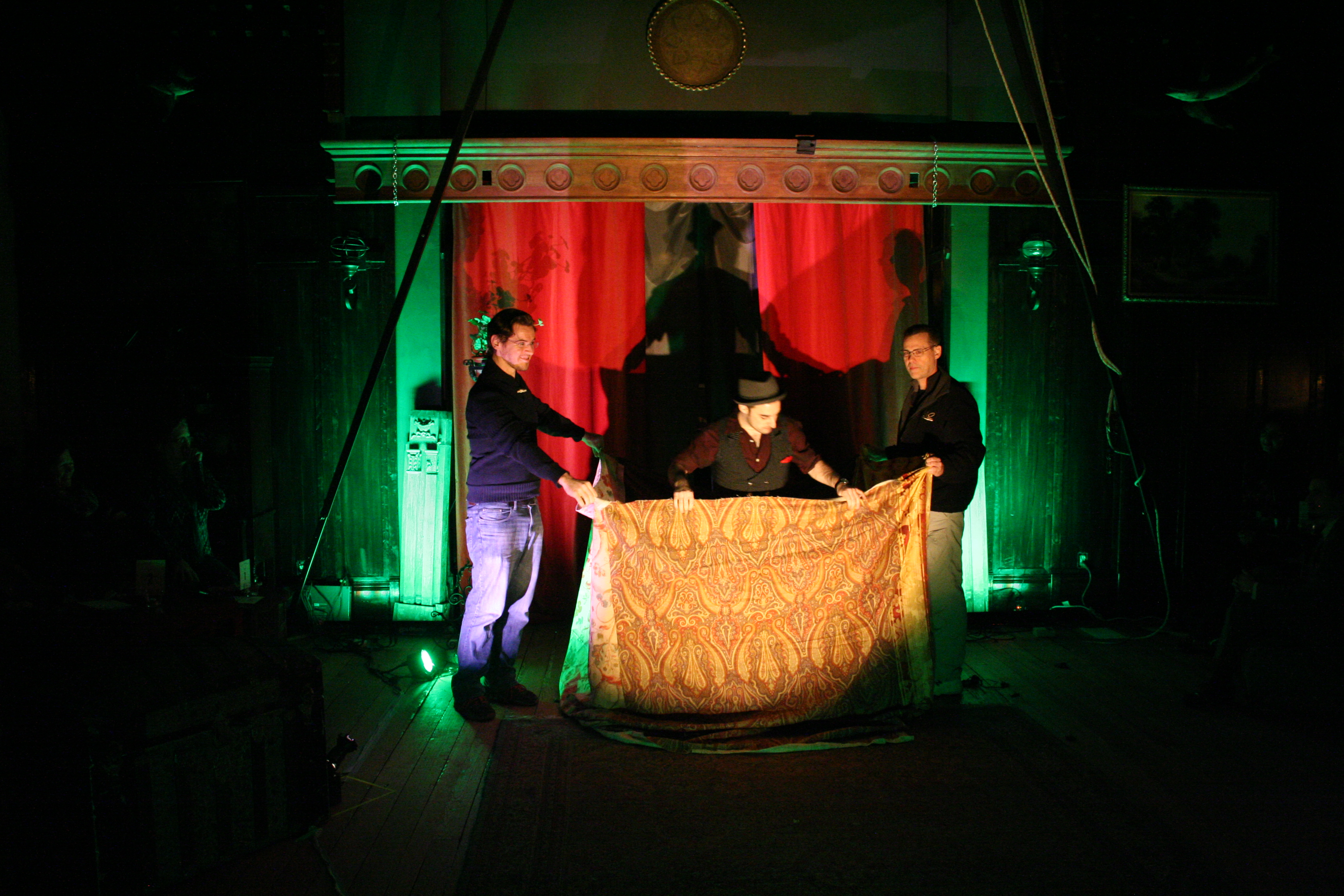 Magician stands with volunteers and a large curtain.