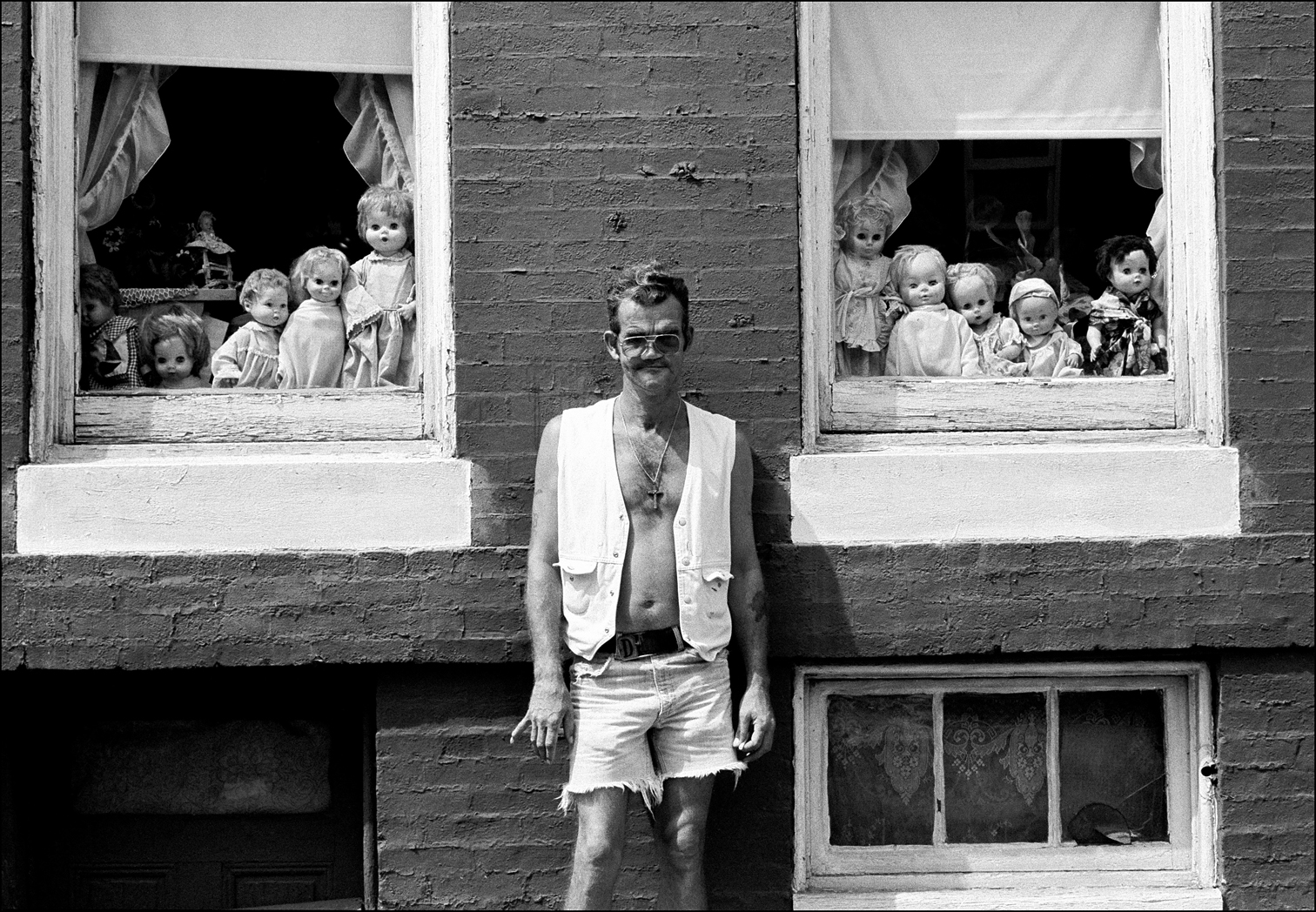 photograph of man with dolls in window