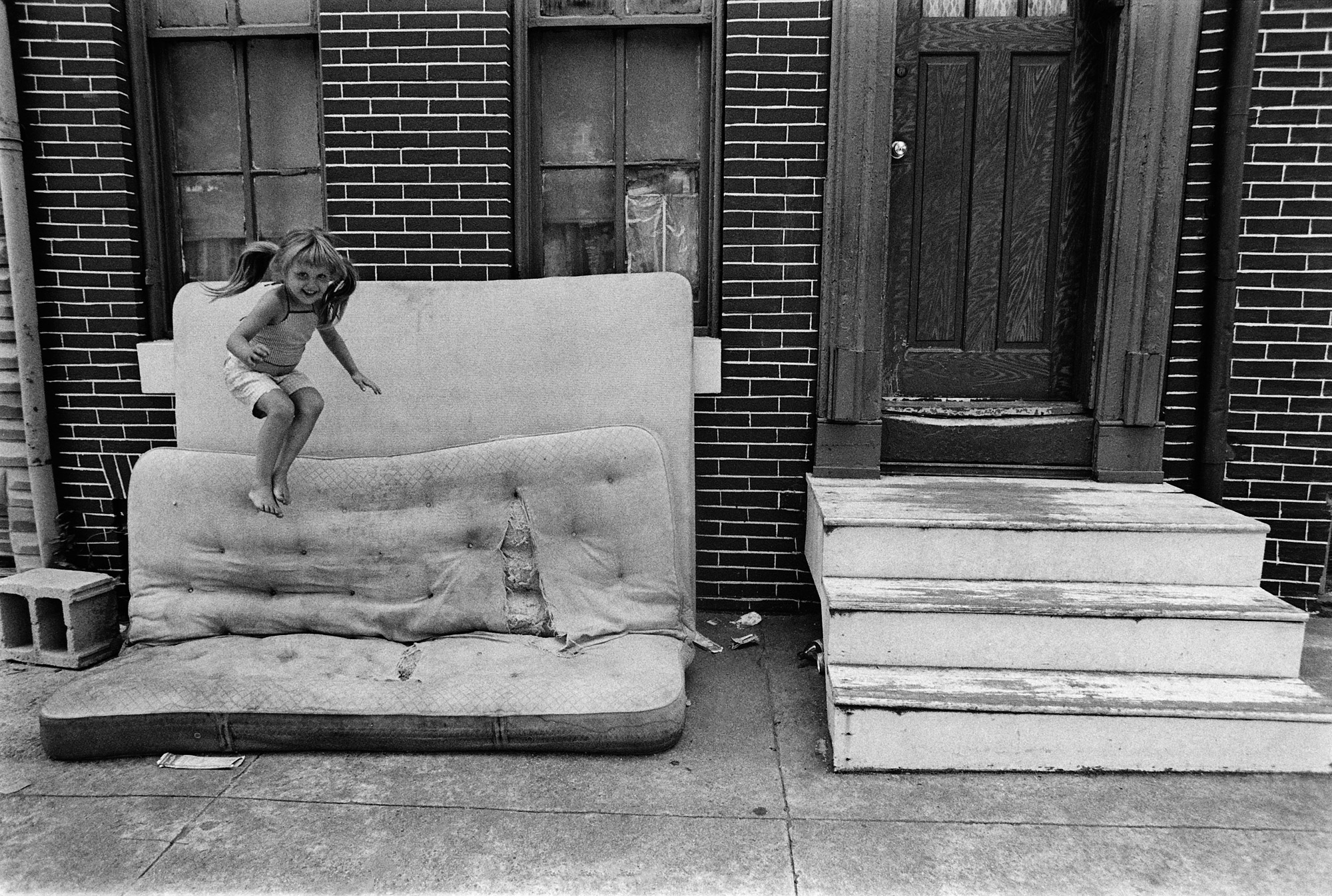 photograph of girl jumping on dirty mattress in Baltimore City