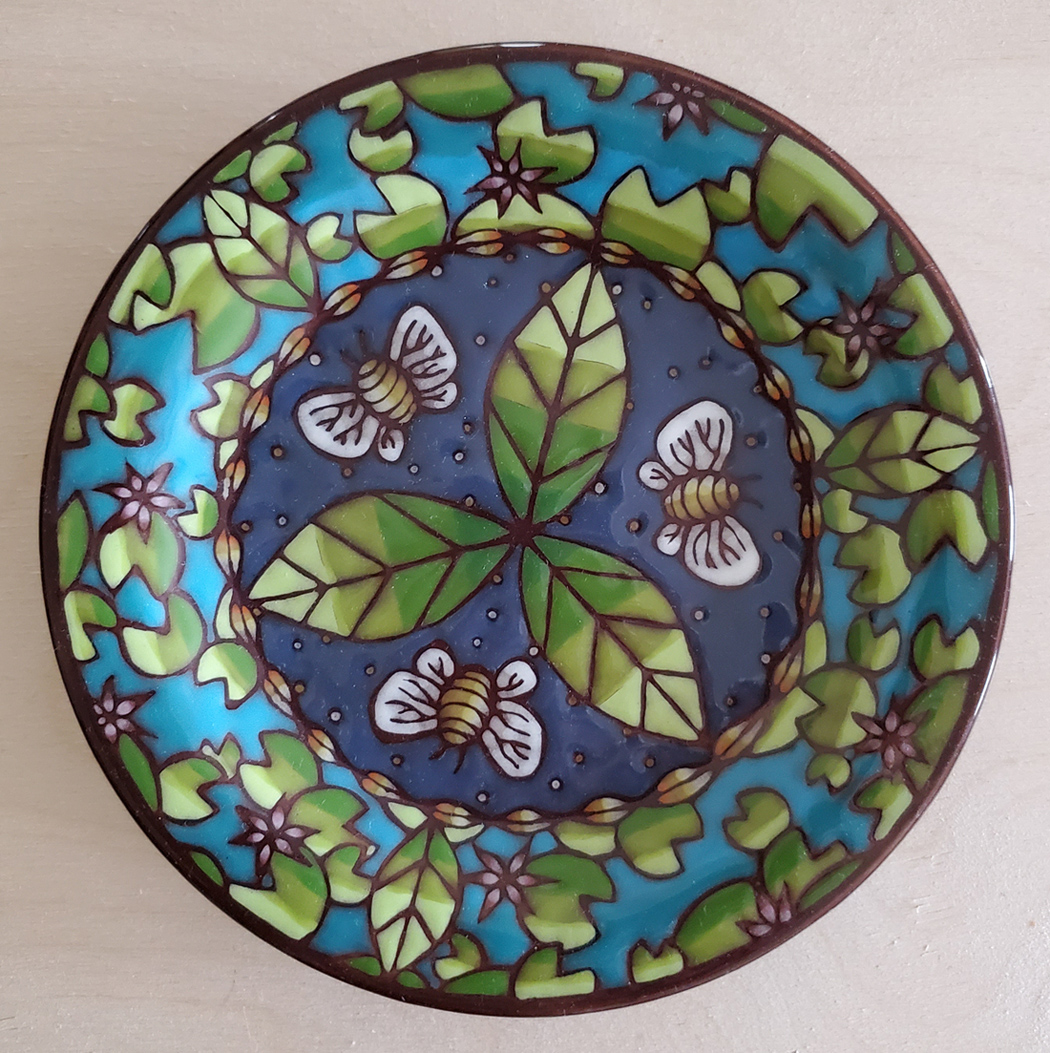 Plate with kaleidoscopic images of bees, leaves, and lilypads 