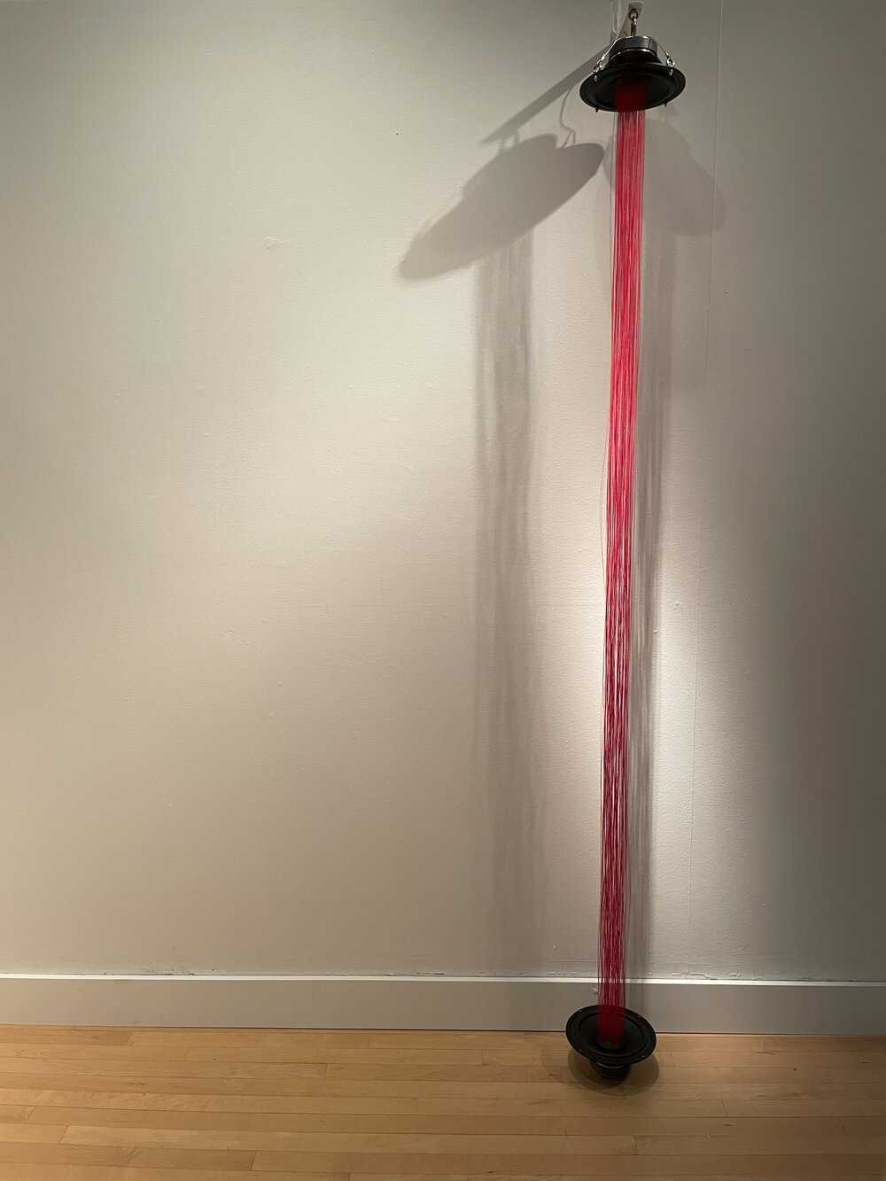 a sculpture consisting of two speakers connected by dozens of red threads, spanning a gallery wall
