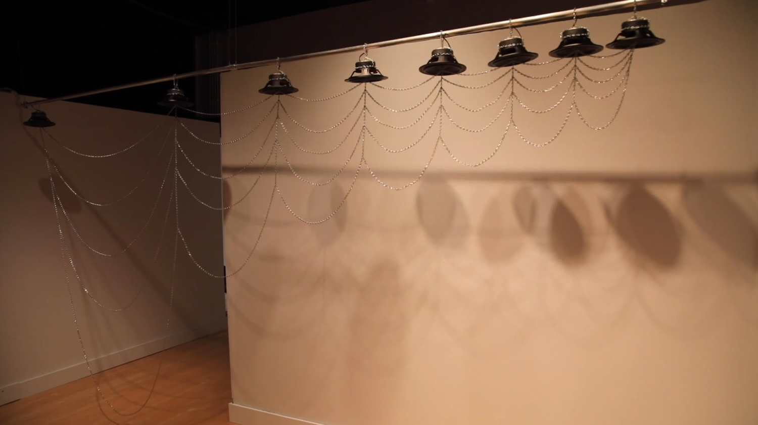 a sculpture consisting of 8 speakers hanging from a bar, connected by chains