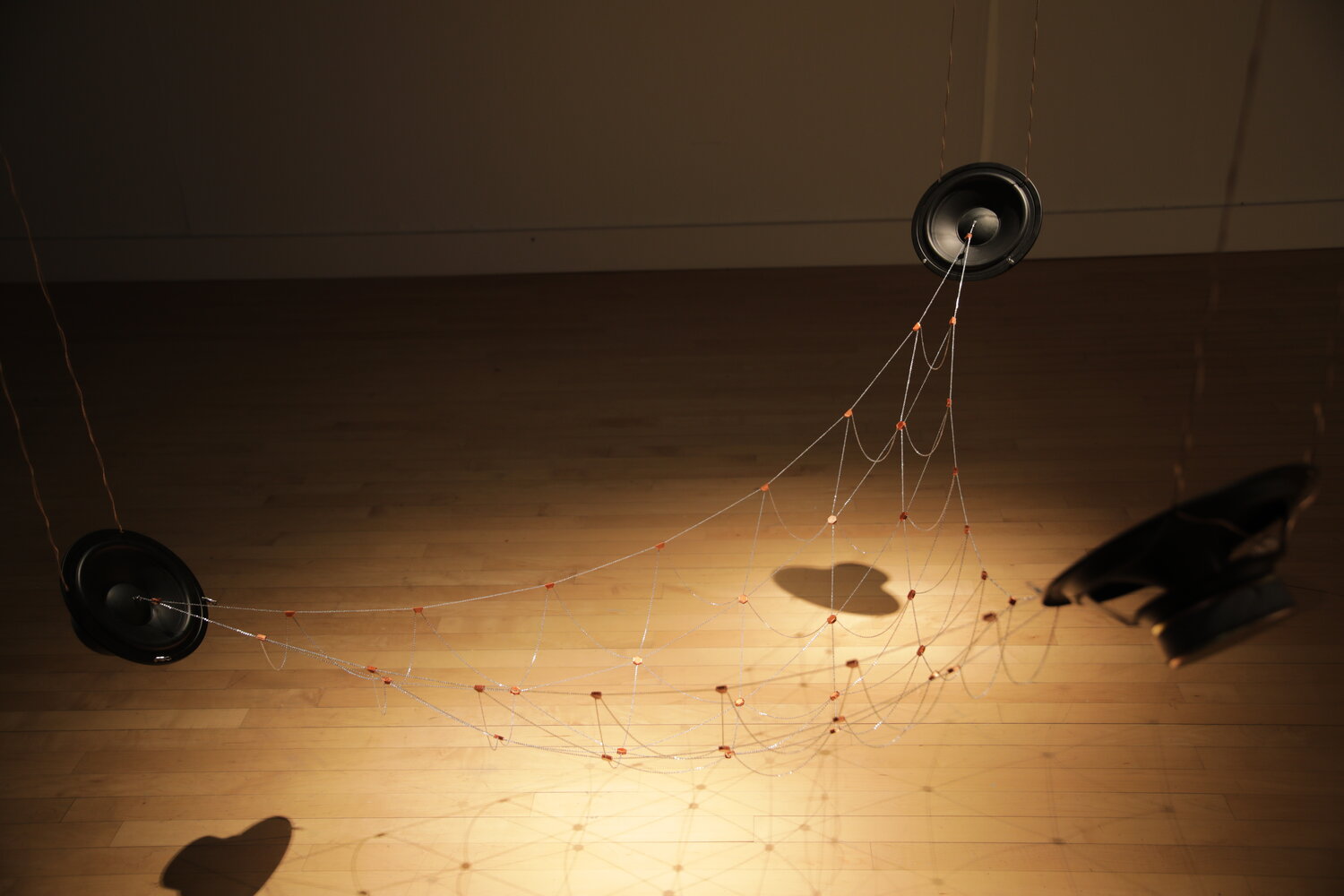 a hanging speaker sculpture consisting of speakers connected by a mesh of fine chain