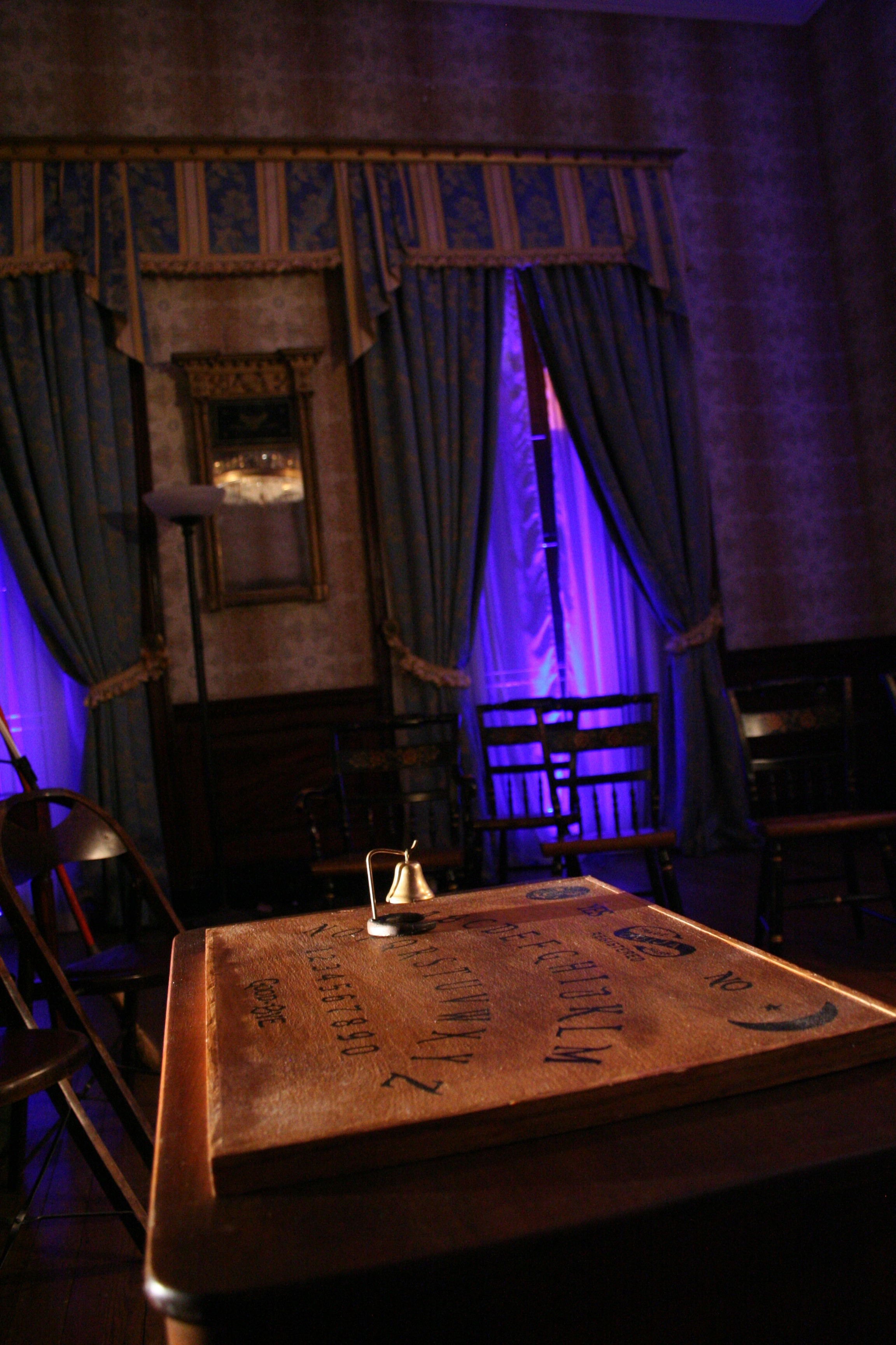 A purple light on curtains in the background, Ouija board and bell in the foreground.