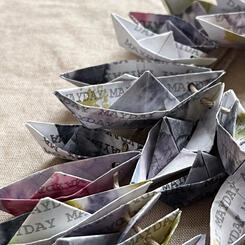Mayday /The Precariousness of Our Predicament- a neckpiece of weathered paper boats imprinted with the repeated message, Mayday.