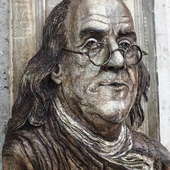 An image of Ben Franklin looking over eyeglasses, carved into a phonebook and painted