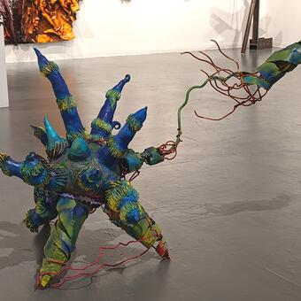 Starfighter , 2022 Sculpture 3.5 ft tall x 6 ft wide x 2 ft deep, ceramic, welded steel and acrylic  This is a ball with starfish- like  or octopus - like arms all around it . one of its arms has jettisoned from its body . Thin steel loops are like blood vessels still attached to the arm and the body. The work is in shades of teal, blues and greens with highlights in hot pink and gold.