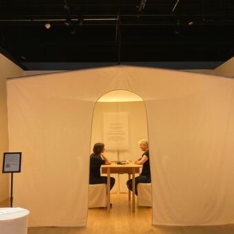 two people sit across a table under a cream colored tent