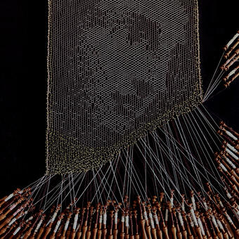 A bobbin lace portrait of a woman's face surrounded by brown wooden bobbins and gold pins