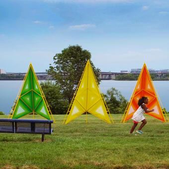 A young girl runs in front of 5 large triangular sculptures 