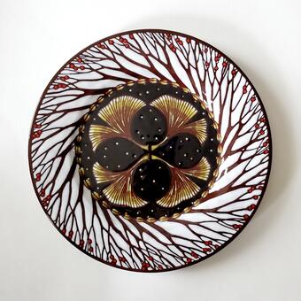 A circular plate with red berries on branches around the rim and 4 ginkgo leaves in the middle against a black starry night background.