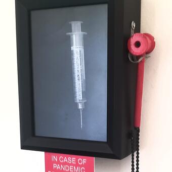 Shadow box with fake Covid 19 vaccination syringe. 