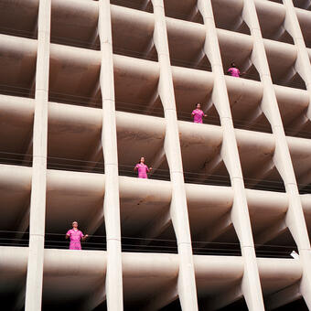 Band Powerwasher standing at the openings of different levels of a parking garage while wearing pink jumpsuits. Photographed from below.