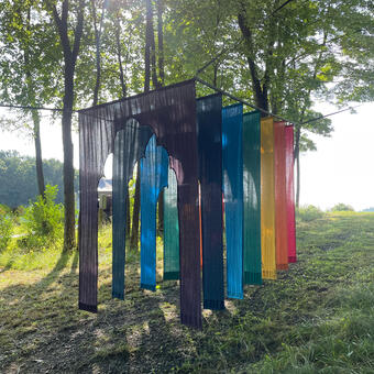 An image of the rainbow gateway installation in the forest, with sun through the trees.