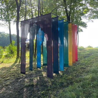 An image of the rainbow gateway installation in the forest, with sun through the trees.