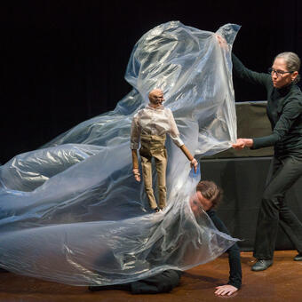 Four puppeteers manipulate a large piece of plastic to represent a tidal wave in a performance.