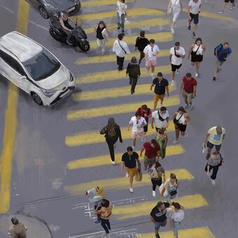 A large group of people are shown form above crossing and yellow crosswalk as cars wait on the left