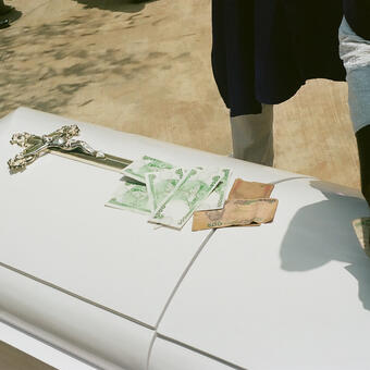 A White Casket with a silver cross with Nigerian currency on the top 