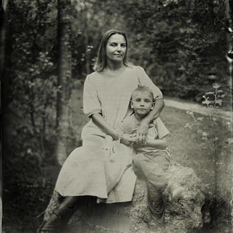 A portrait of a mother and her 6-year-old son; they are sitting on the rock and mother had her arm wrapped around the boy.  Both are looking at the camera.  Full body; wet plate collodion photograph