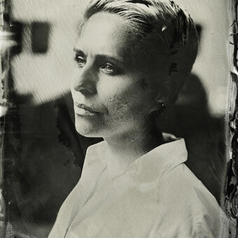 A wet plate collodion portrait of a woman with short blond hair in 3-quarter view; there is collodion artifact around the edges of the image.