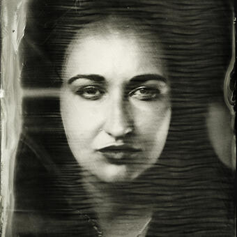 A symmetrical close up of a woman's face, looking at the viewer; wet plate collodion photograph artifacts around the edges of the image