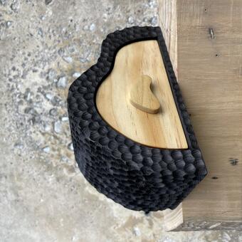 An organically shaped wood box with a single drawer that pulls outward. The box body is carved with a pattern of large, circular indentations and dyed black; the drawer is natural wood grain.