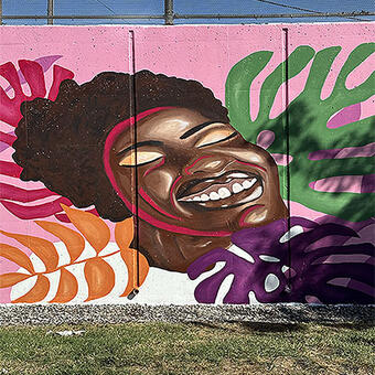 image of radiant black woman smiling. She is surrounded by multi-colored monstera leaves
