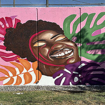 image of radiant black woman smiling. She is surrounded by multi-colored monstera leaves