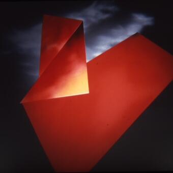 This is a glossy photograph of flat bright red images in a sky like setting with clouds.