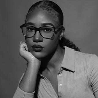 Monica Ikegwu, wearing dark glasses, looking directly at viewer with chin resting on right hand