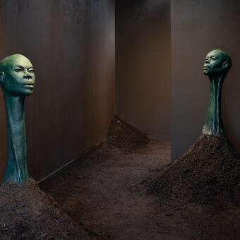 Three green figurative sculptures growing from mounds of dirt