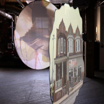 two floating portals are suspended in an industrial space. One portal opens to a video of row homes and the other is indistinct. 