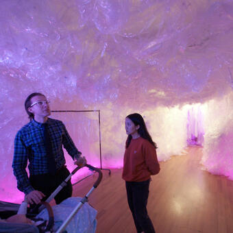 Photo of the installation with the glow of the neon lighting and 2 adults and a bably in a stroller.