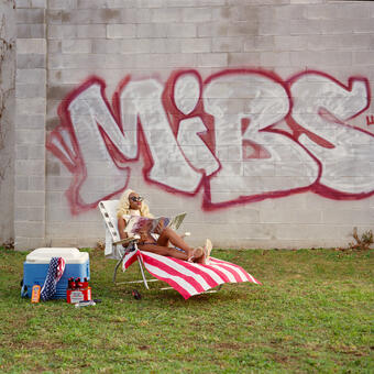 Woman in a breast plate, tanning in a beach chair in vacant lot.