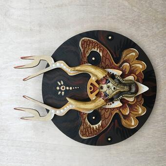 A red, black, and tan wooden symmetrical sculpture with a horned creature in the center.