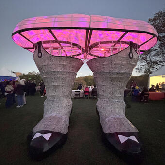 Illuminated sculpture of a giant hairy womans legs in heels and glowing flowing skirt. air meets the earth. Pop meets Myth.