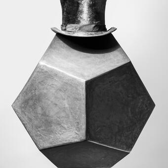 Abstract monochrome portrait of a black geometric form made from papermache wearing a large vintage top hat -- size 7 1/4  -- photographed in studio against a gray background