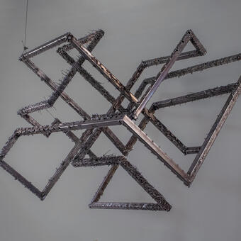 Steel twists in midair, tubes interlocking in angular, unpredictable loops. Its textured surface recalls an artifact pulled from the deep sea.