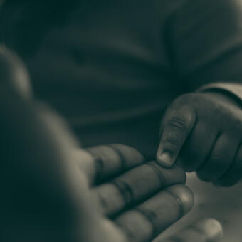 Monochromatic photo of father holding out his hand for his baby son. The baby touches the hand with his finger. Key zoom is emphasized on the hands