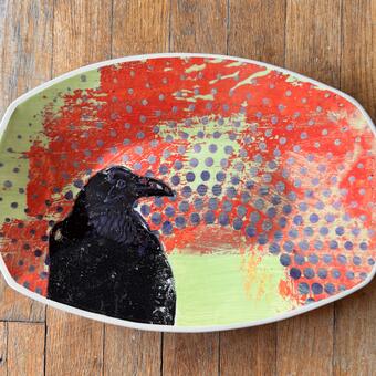 Black raven on a ceramic platter with orange, chartreuse and purple dot arch pattern.