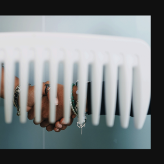 Two hands clasp together behind the wide teeth of a large white comb.