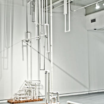 A system constructed of PVC pipe, mimicking systems of infrastructure, suspended from the ceiling and extruding fro the walls and floor.