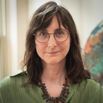 1:58 AMClaude responded: Woman with shoulder-length brown hair and wire-frame glasses, wearing a green linen shirt and a beaded necklace, photographed in front of an abstract artwork.Woman with shoulder-length brown hair and wire-frame glasses, wearing a green linen shirt and a beaded necklace, photographed in front of an abstract artwork.
