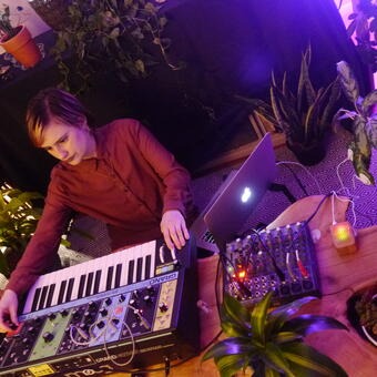 woman playing a synthesizer surrounded by plants