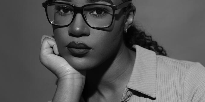 Monica Ikegwu, wearing dark glasses, looking directly at viewer with chin resting on right hand