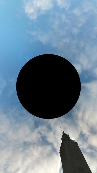 Image of the sky with a black hole in the center and the top of a minaret in the bottom right corner