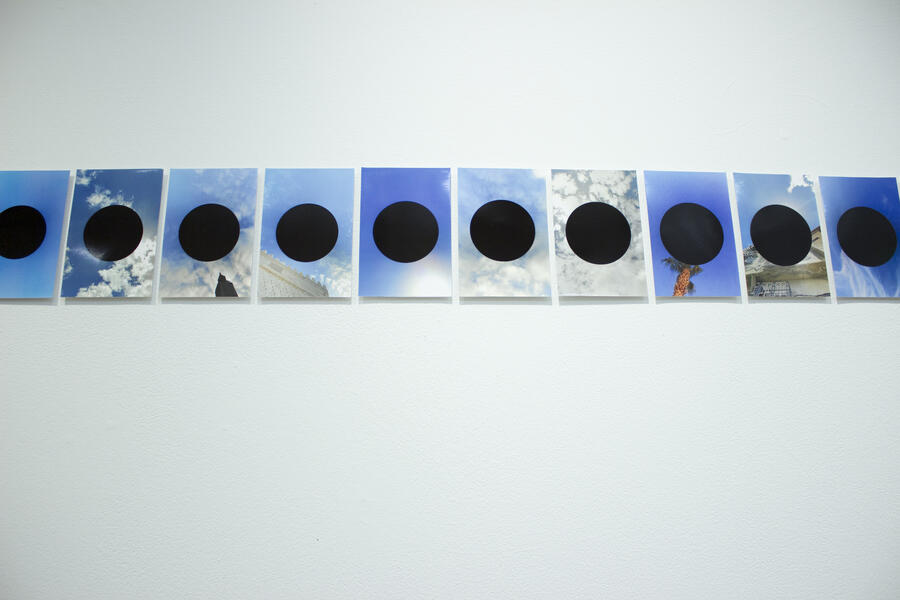 Row of photographs with a black hole in the center of each on a white wall