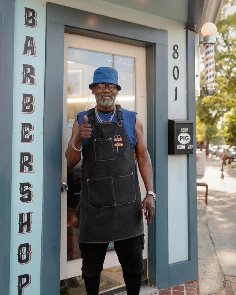 A man poses for a portrait outside his barbershop in Pigtown.